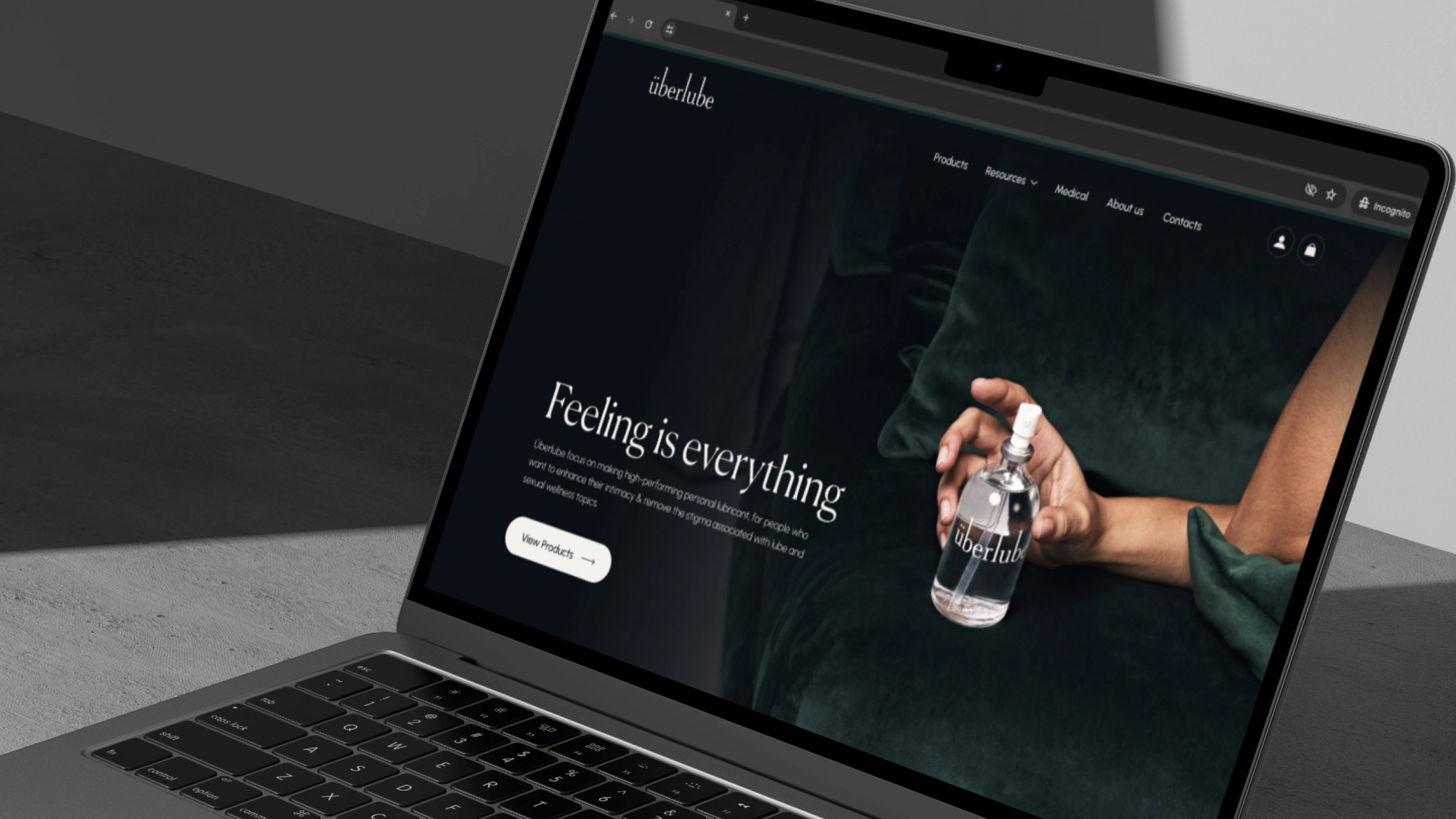 The Überlube homepage on a laptop: Feeling is everything, with a hand holding the glass bottle